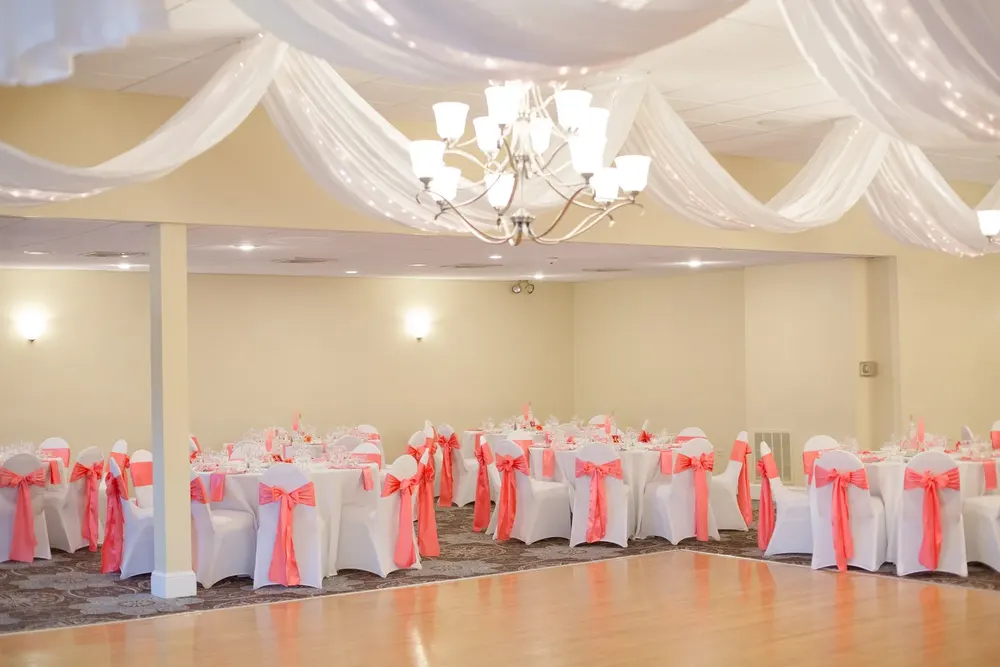 A ballroom set with round tables and coral sashes